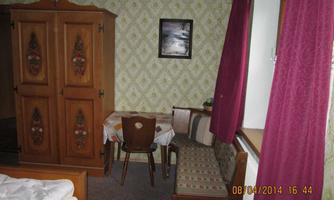A simple room with a wooden wardrobe, a table, and chairs. The walls are decorated with a floral pattern and a picture.