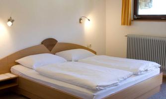 A simple bedroom with a double bed and two nightstands. There is a window with curtains and a heater on the wall.