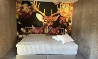 A cozy bedroom with a large bed and colorful pillows. The wall is decorated with an impressive stag motif and floral elements.