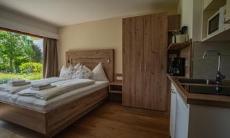 A modern bedroom with a double bed and wooden furniture. Through the window, one looks out onto a green landscape.