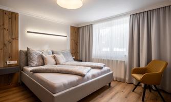 A modern bedroom with a comfortable bed and cozy pillows. There is a chair and large windows that let in daylight.