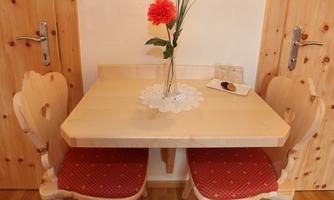 A beautiful table made of light wood with two chairs and a vase of flowers in the middle. On the table is a small plate with pastries.