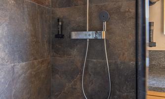 A modern shower with an elegant fixture. The walls are clad in dark tiles.