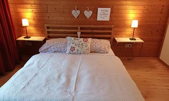 A cozy bedroom with a large bed and wooden wall paneling. There are lamps and a few decorative elements on the nightstands.