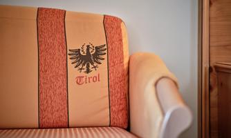 An inviting sofa with an orange cover and the coat of arms of Tyrol. The elegant design offers a cozy look.