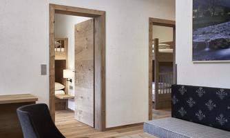 A modern room with wooden details and two open doors. In front, there is a comfortable chair and a couch.