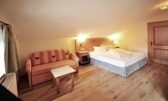 A cozy room with a large bed and a sofa. The warm colors and the wood create an inviting atmosphere.