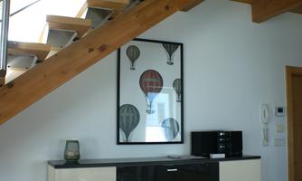 A modern interior with a wooden staircase and a white sideboard. A piece of artwork featuring balloons hangs on the wall.