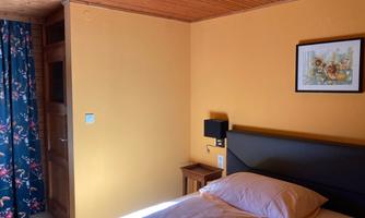 A cozy bedroom with a large bed and orange walls.  
Windows with blue curtains and a small table next to the bed.