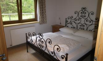 A cozy bedroom with a wrought-iron bed and two pillows. Large windows let in plenty of daylight and offer a view of nature.