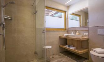 A modern bathroom with a glass shower and a wooden vanity. Plenty of natural light from large windows.