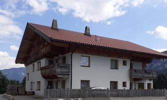 A traditional Bavarian house with a red tile roof. It has balconies and a beautiful view of the mountains.