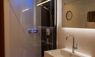 A modern bathroom with a walk-in shower and stylish lighting. The wooden surface and the white sanitary fittings give an elegant look.