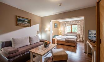 A cozy hotel room with a sofa, a table, and a sleeping area. Bright walls and large windows create an inviting atmosphere.