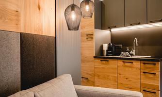Modern kitchenette with wooden cabinets and stylish pendant lights. Cozy seating area with a bright sofa in the foreground.
