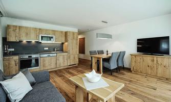A modern living and dining room with a wooden kitchen unit. The room is bright and friendly furnished, with wooden flooring and a cozy sofa.