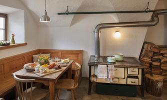 A cozy kitchen with a wooden table, chairs, and a vintage stove. Fresh ingredients and dishes are decoratively arranged on the table.
