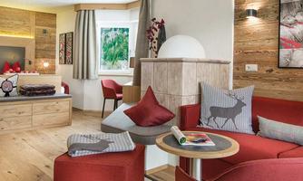 A cozy living room with a red sofa and a round table. There are wooden elements and large windows that let in plenty of light.