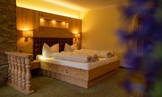 A cozy bedroom with a wooden bed and large pillows. The warm lighting and rustic style create an inviting atmosphere.