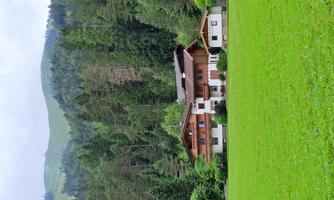 A beautiful house surrounded by green meadows and forests. Gentle hills can be seen in the background.