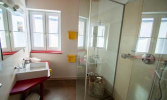 A modern bathroom with a glass shower and a sink. Bright windows provide plenty of daylight.