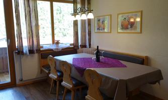 An inviting dining area with a large table and wooden chairs. The table is decorated with a purple tablecloth, and large windows provide plenty of daylight.