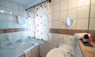 A modern bathroom with a bathtub and white tiles. A colorful curtain with a floral pattern lets in natural light.