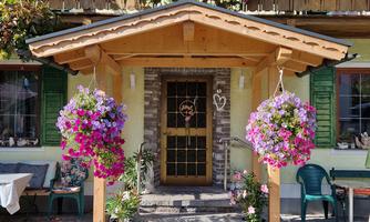 An inviting entrance area with blooming plants and colorful flower boxes. The wooden structure and the shutters give the house a charming, rustic character.