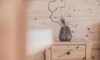 A cozy room with wooden walls. On a wooden table sits a vase with decorative branches.