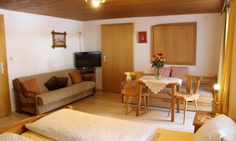 A cozy living room with a sofa, a table, and chairs. There is also a TV and a bouquet of flowers on the table.