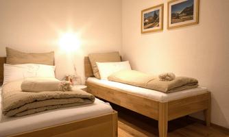 A cozy bedroom with two single beds and warm bedding. Two pictures of mountains are hanging on the wall.
