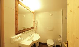 A modern bathroom with a large mirror and a sink. The walls are light tiled, and there is a toilet as well as a towel rack.