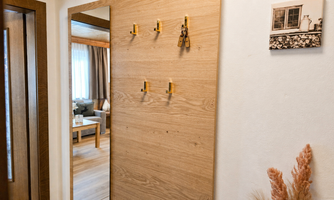 A beautiful hallway with a wooden panel and hooks for storage. In the background, you can see a cozy living area with soft furniture.