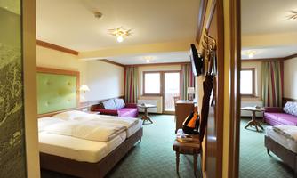 A bright hotel room with two beds, a cozy seating area, and large windows. The color scheme is friendly and inviting.