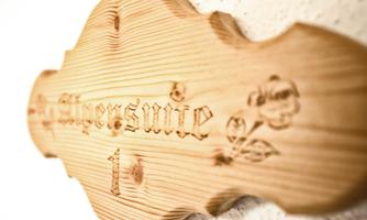 A wooden sign with the inscription "Alpensuite 1" and intricate floral patterns. It is attached to a wall and conveys a rustic atmosphere.