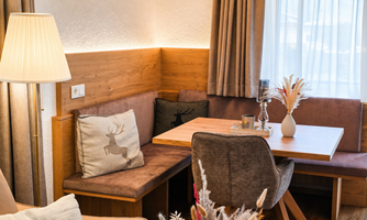 A cozy seating area with a wooden log table and upholstered benches. On the table, there is a vase and decorative grain.