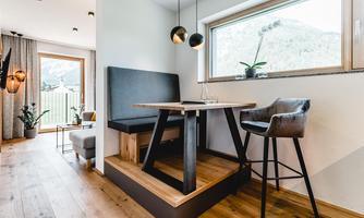 A modern dining room with a cozy bench and an elegant table. Large windows let in plenty of daylight and provide a view of the landscape.