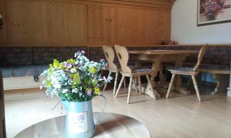 A cozy room with wooden paneling and a dining table. In the foreground, there is a blooming plant in a metal watering can.