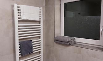 A modern bathroom with a towel warmer and large tiles. Two towels are ready next to the window.