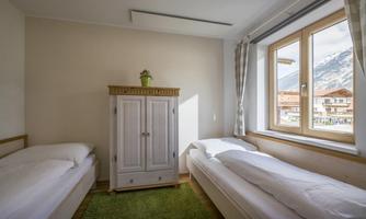 A bright bedroom with two single beds and a white wardrobe. Through the window, there is a beautiful view of the mountains.
