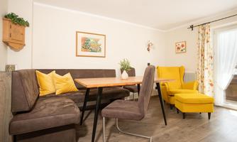 A cozy living area with a wooden table and modern chairs. Yellow armchairs and a bright window front create a friendly atmosphere.