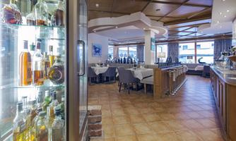 An elegant restaurant with tables and chairs in an inviting atmosphere. In the background, there is a bar with a selection of bottles visible.