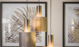 Modern lamps hang in front of pictures of palm leaves. The warm lighting creates an inviting atmosphere.