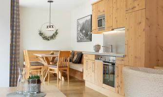 A cozy kitchen with wooden cabinets and a wooden dining table. The room design is bright and inviting with modern appliances.