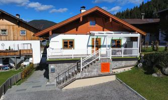 A modern house with an orange roof and friendly windows. The entrance is accessible via a staircase and a small balcony.