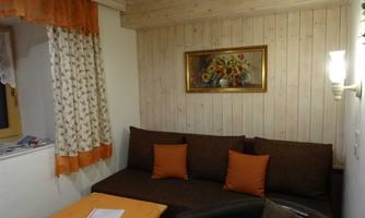 A cozy living area with a brown couch and orange cushions. A painting hangs on the wall and the decor is bright and inviting.