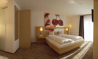 A modern hotel room with two beds and a large window. An artwork featuring cherries and lips hangs on the wall.
