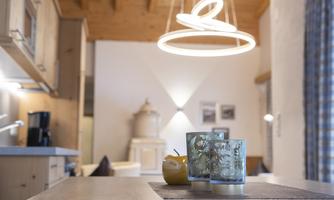 A modern kitchen with wooden ceilings and a round light. On the table, there are three decorative candles and a yellow fruit.