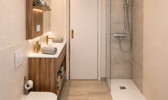 A modern bathroom with wooden shelves and elegant fixtures. The shower is designed with an open concept, and fresh towels are available.