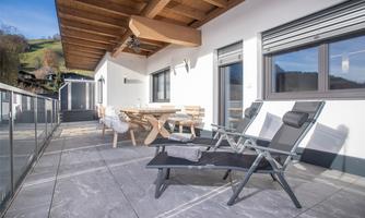 A modern terrace with a seating area and loungers. The space is bright and inviting, surrounded by green nature.
